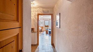 Un pasillo con puertas de madera, suelo de baldosas y vistas a un salón con sofá y una mesa.