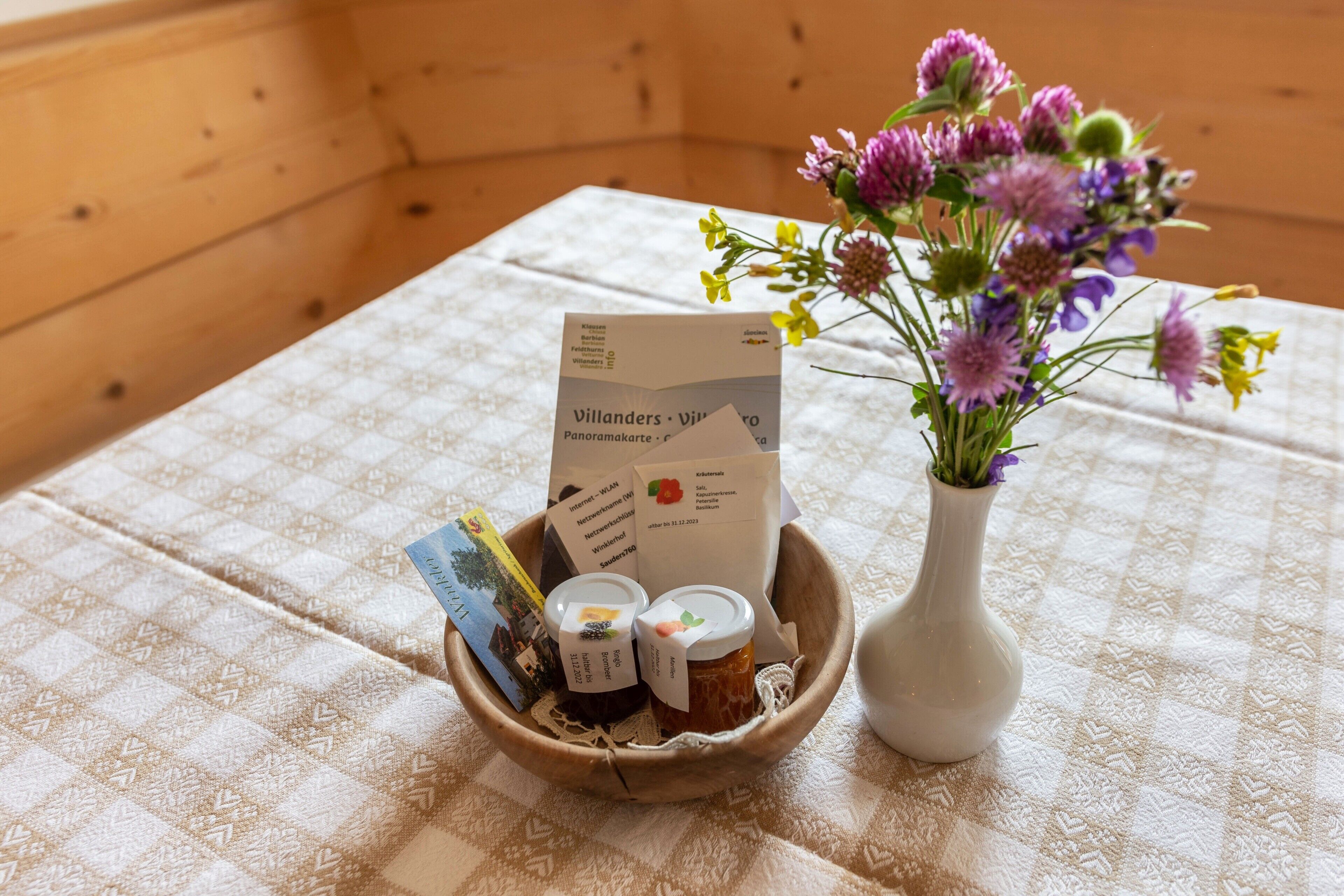 Un intérieur en bois avec une table sur laquelle se trouvent un bol rempli d’objets, un vase avec des fleurs et une carte.