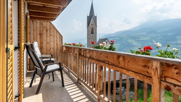 Un balcón de madera con vistas a una iglesia y montañas.