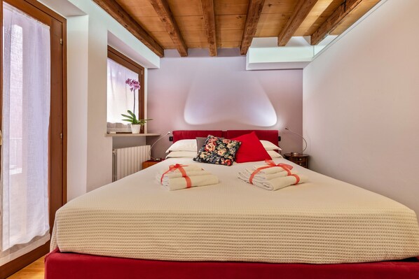 Une chambre d’hôtel avec un grand lit, une fenêtre avec des rideaux, une plante en pot et un plafond en bois.