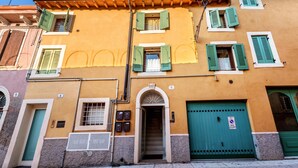 Un bâtiment avec une porte verte, une enseigne portant le chiffre « 6 », et une fenêtre avec des volets verts.