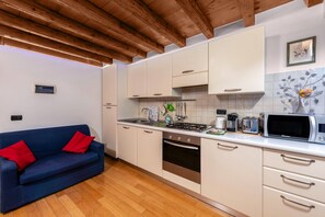 Une cuisine de taille réduite avec des meubles blancs, un canapé bleu et un plafond en bois.