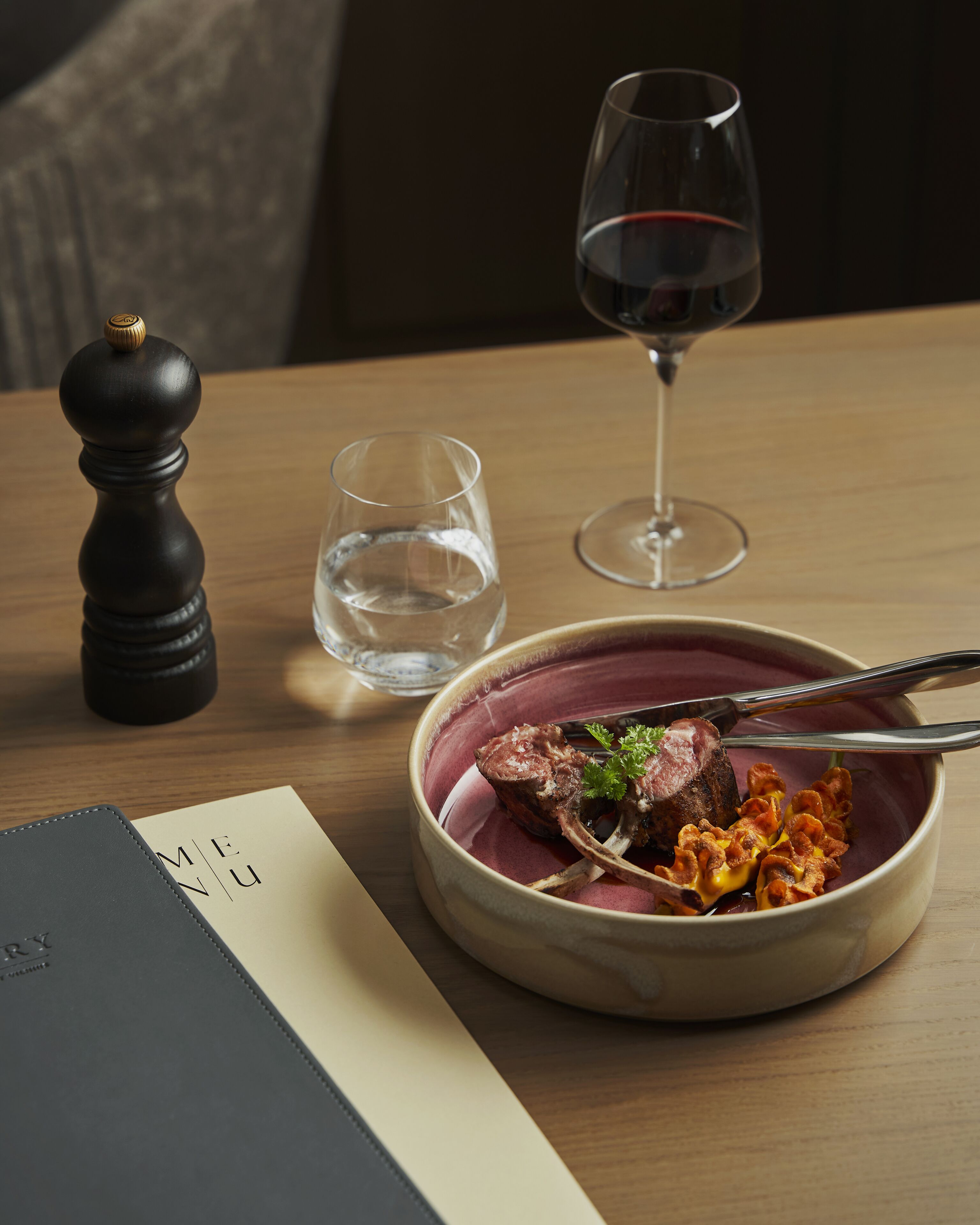 A dining table with a bowl of food, a wine glass, a pepper shaker, and a menu.