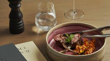 A dining table with a bowl of food, a wine glass, a pepper shaker, and a menu.