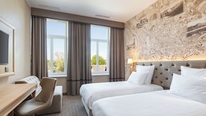 Habitación de hotel con dos camas, un escritorio, una silla y un ventanal con cortinas.