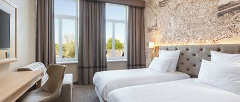 A hotel room with two beds, a desk, a chair, and a large window with curtains.
