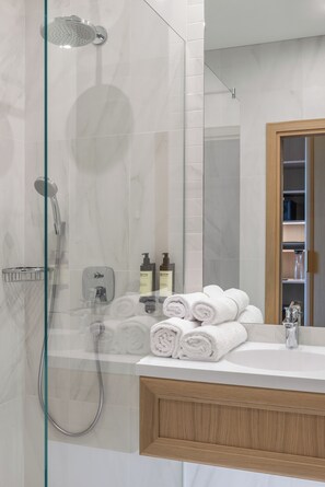 A modern bathroom with a glass-enclosed shower, a wooden vanity, and neatly rolled towels. - CALVARY Hotel & Restaurant Vilnius (Vilnius)