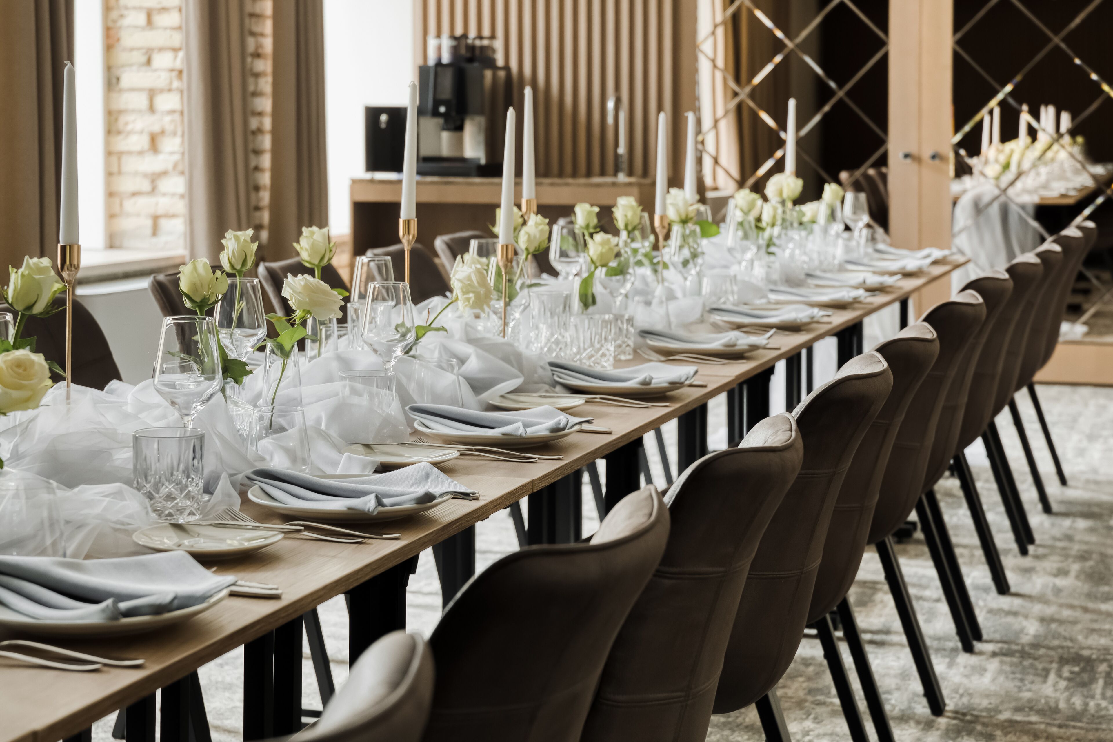 Una larga mesa de comedor cubierta con manteles blancos, copas y flores blancas.