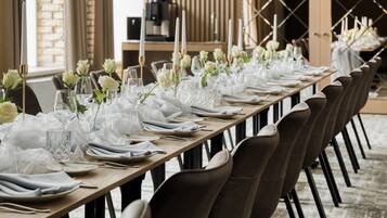 Una larga mesa de comedor cubierta con manteles blancos, copas y flores blancas.