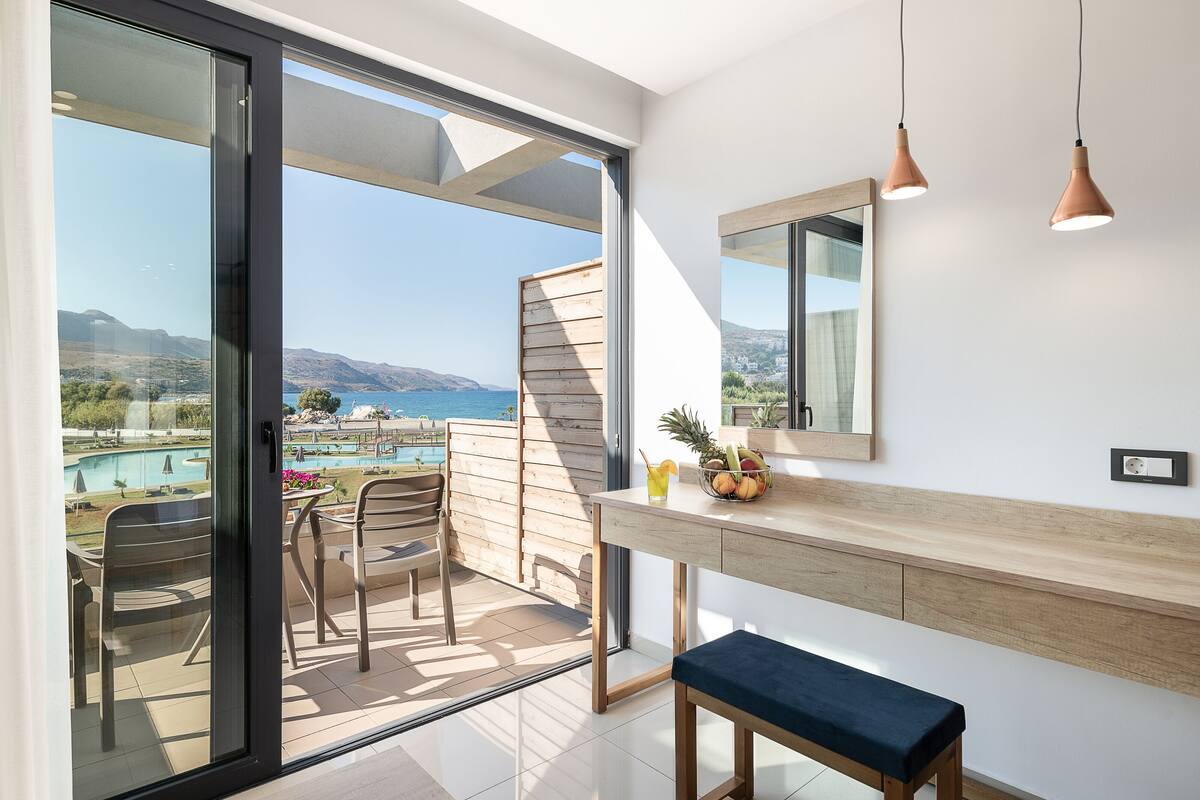 Ein Balkon mit Blick auf ein Schwimmbad und Berge, ein Holztisch mit Stühlen und Pendelleuchten.