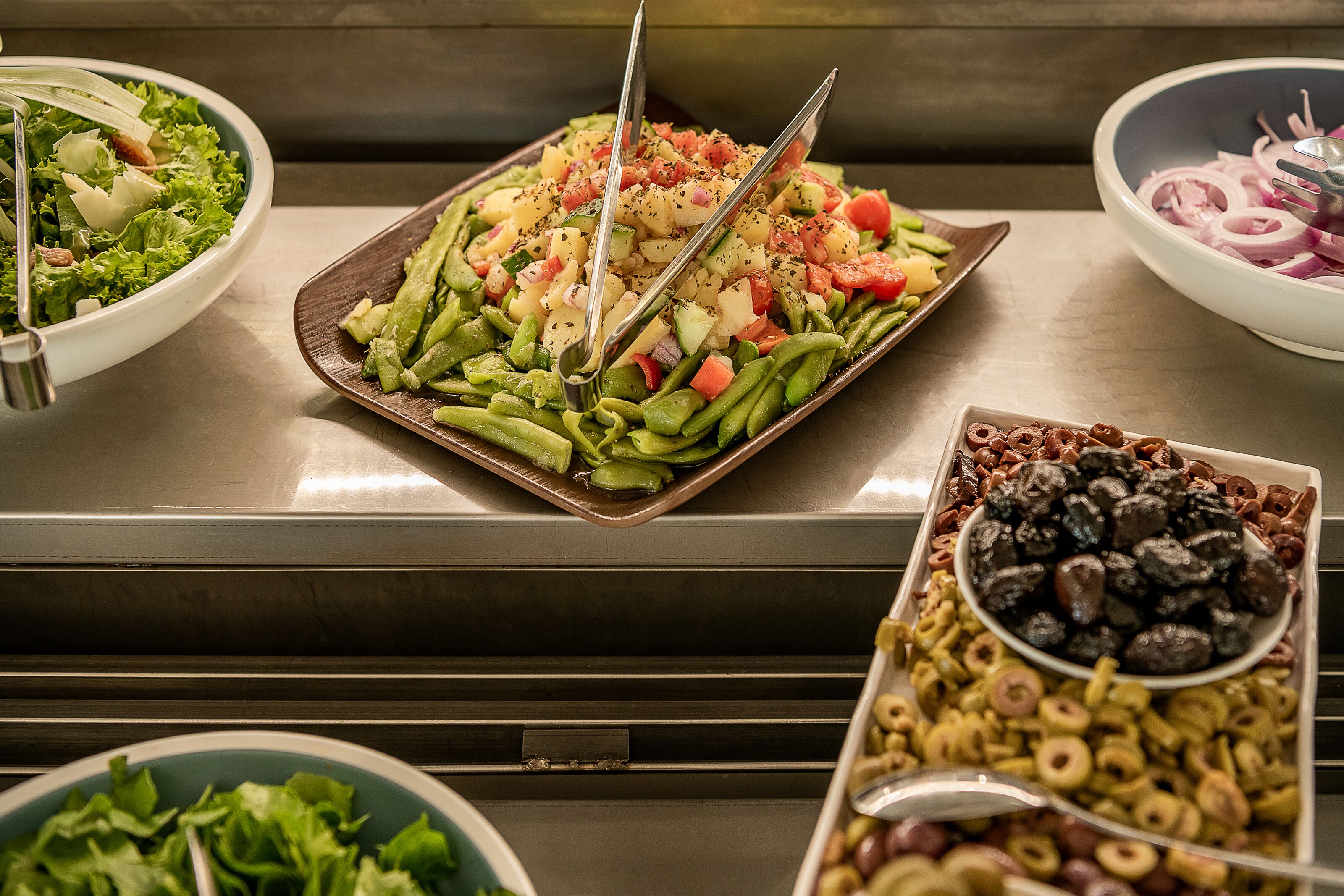 A buffet with various dishes including a salad, green beans, and olives.