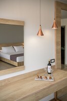 Une chambre d’hôtel moderne avec un lit doté d’une tête de lit en bois, un grand miroir et une console en bois sur laquelle sont posés une bouteille de vin et des verres.