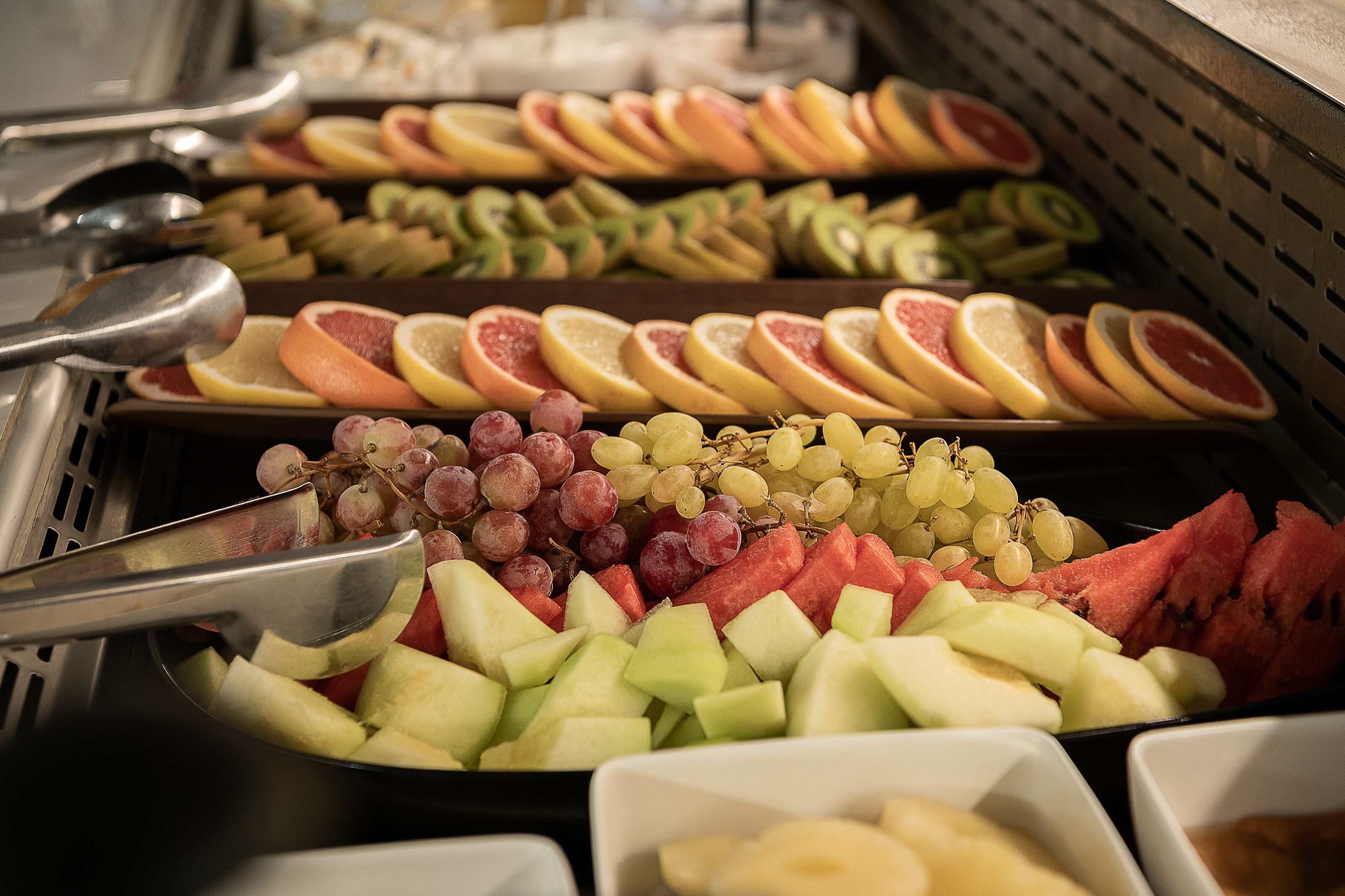 A buffet with various fruits and vegetables, including sliced apples, grapes, and watermelon.