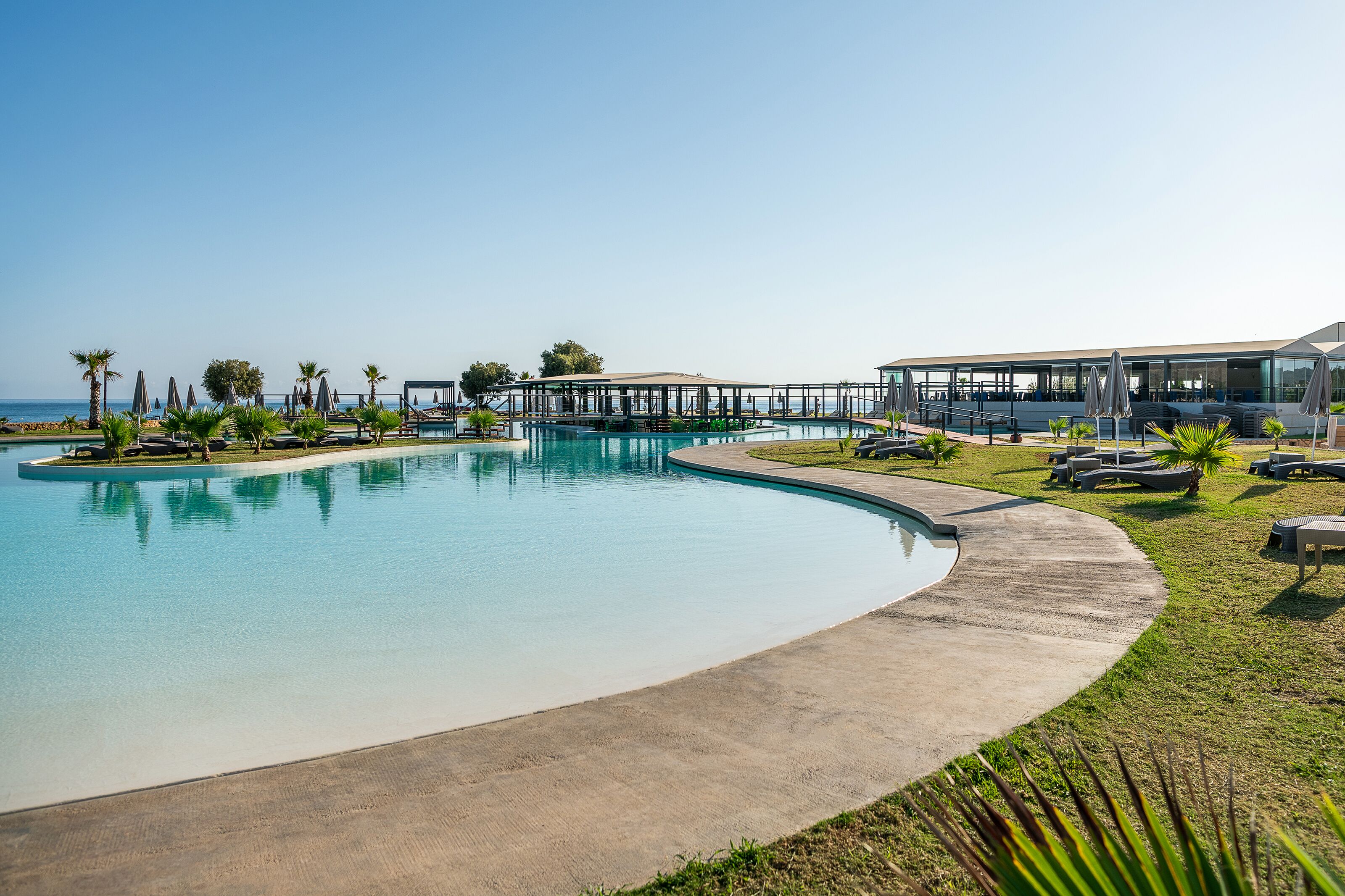 A pool area with a curved edge, lounge chairs, and a covered seating area.