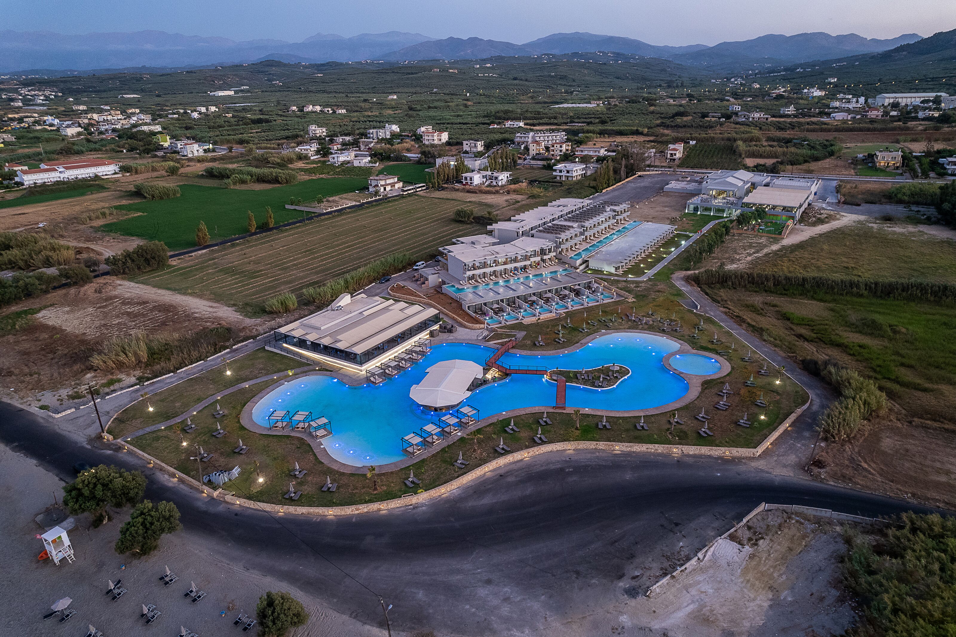 An aerial view of a resort with multiple swimming pools, a large building, and surrounding greenery.