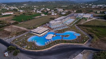 An aerial view of a resort with multiple swimming pools, a large building, and surrounding greenery.