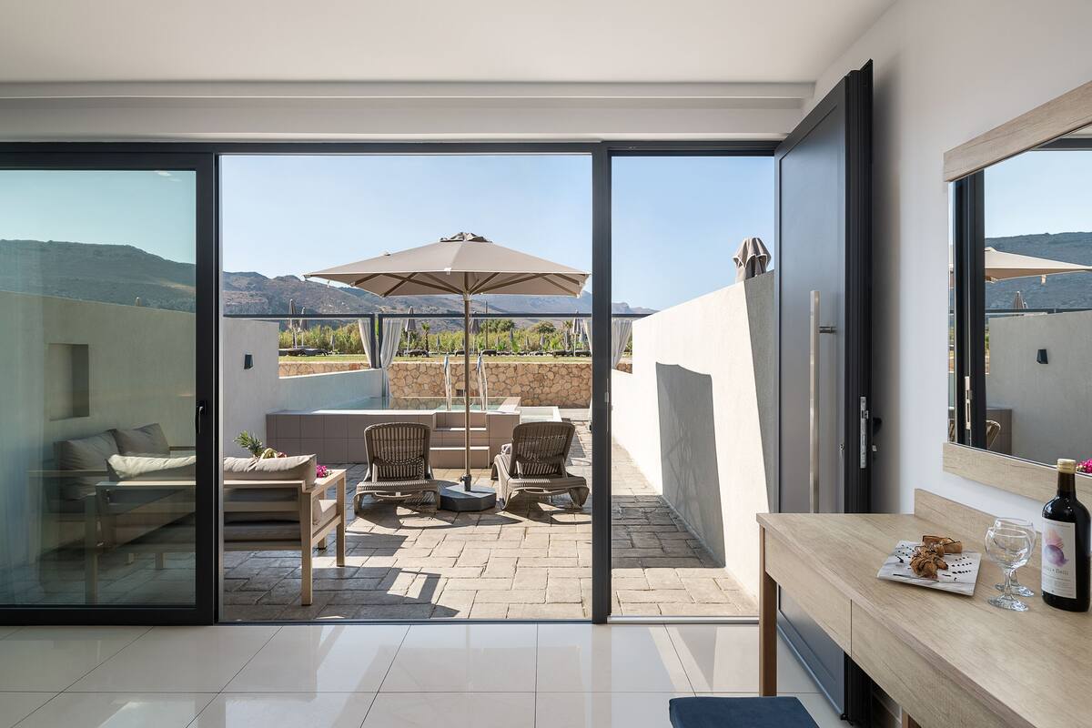Ein modernes Zimmer mit einer Schiebetür zu einer Terrasse, die einen Tisch, Stühle und einen Sonnenschirm bietet.