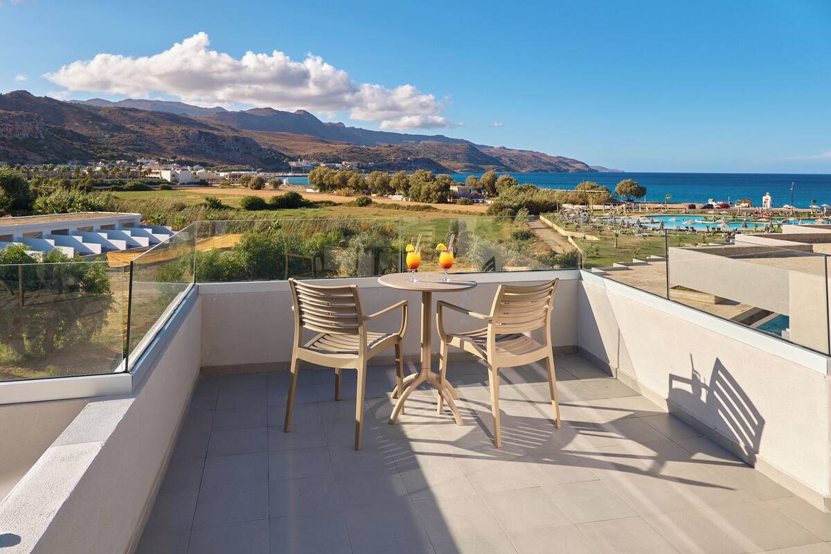 Ein Balkon mit zwei Stühlen und einem Tisch, mit Blick auf einen Pool und Berge.