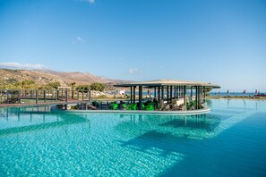 A floating bar with green chairs and umbrellas, surrounded by a pool with clear blue water, and a view of distant mountains. - Galini Palace Resort Hotel - All Inclusive (Platanias)