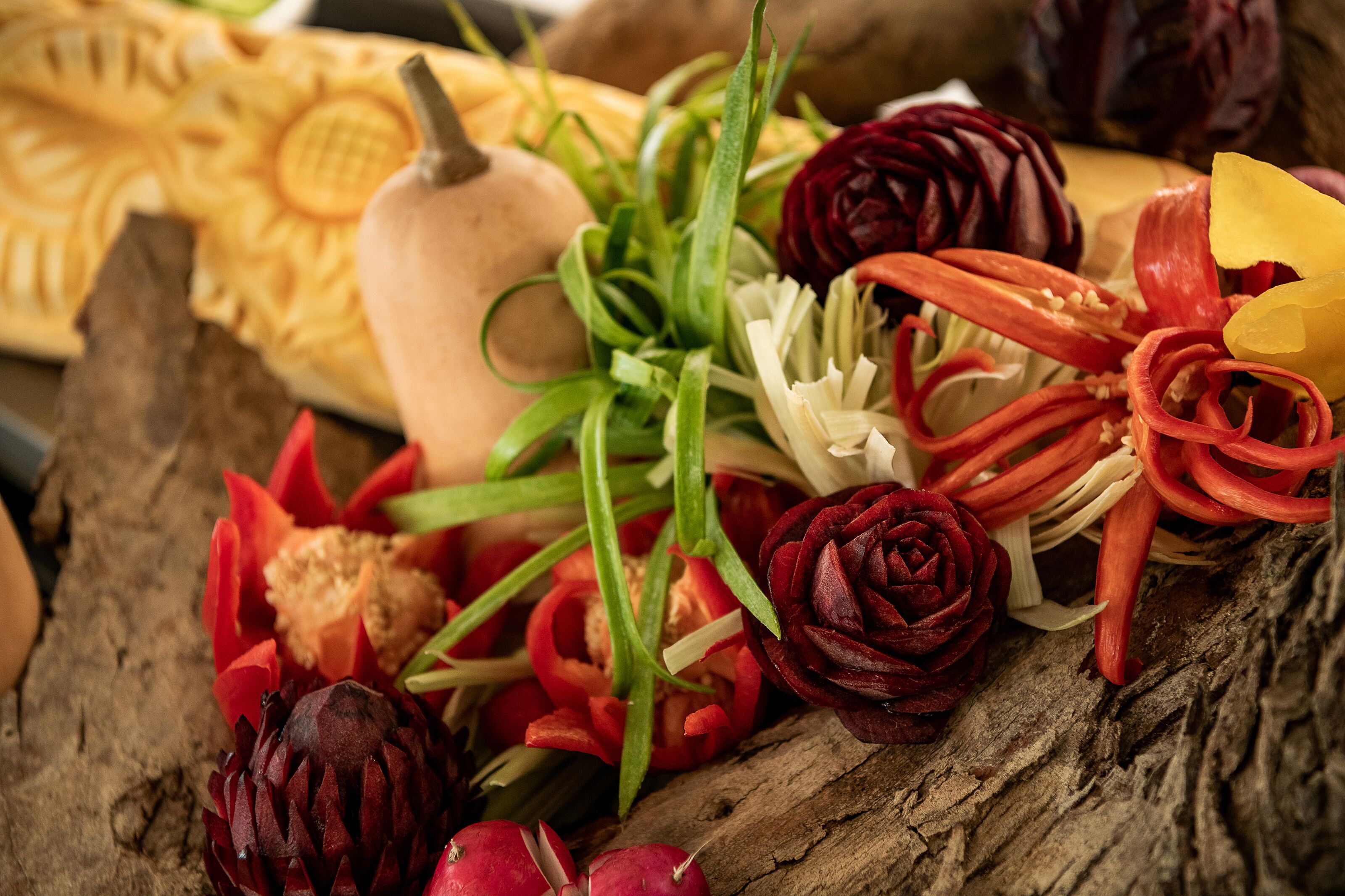 A variety of vegetables and fruits, including artichokes, red peppers, and a pumpkin, arranged on a wooden surface.