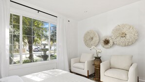 Une chambre dotée d’une grande fenêtre, de deux fauteuils, d’un lit et d’œuvres d’art décoratives accrochées au mur.