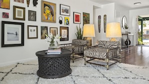 Un salon moderne avec un tapis à poils longs blanc, une petite table d’appoint ronde noire, deux fauteuils à motifs zébrés, un canapé et un grand miroir.