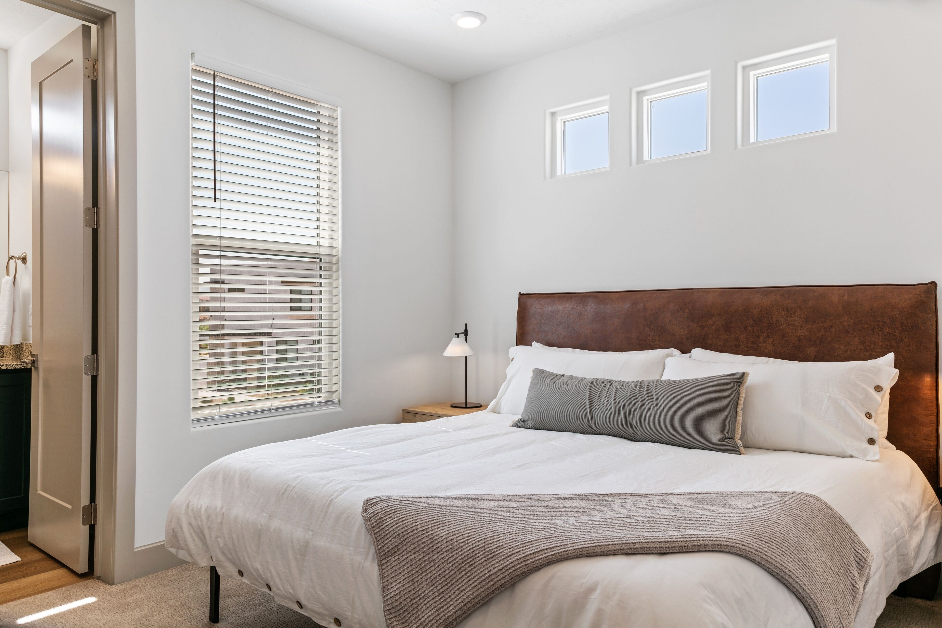 A bedroom with a large bed, a nightstand, a lamp, and a window with blinds.