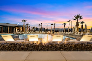 Relax by the pool surrounded by palm trees and lounge chairs, with a fire feature nearby.