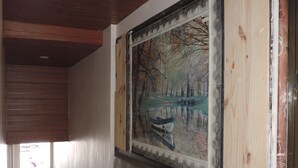Un pasillo con un cuadro grande de un paisaje sereno, que muestra un barco en un lago, paneles de madera en las paredes y una puerta entreabierta al final.