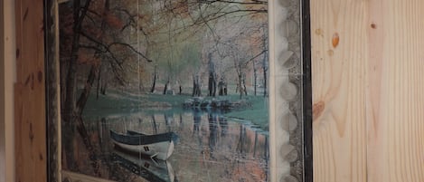 A framed painting of a serene lakeside scene with trees and a boat.
