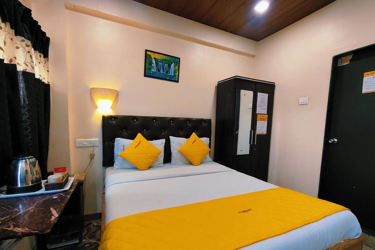 A hotel room with a bed, a nightstand, a lamp, a wardrobe, and a painting on the wall.