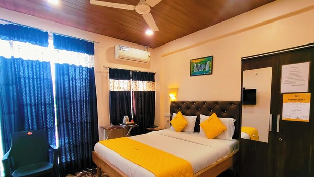 Una habitación de hotel con cama, escritorio, silla, aire acondicionado, lámpara, un cuadro y una puerta con un cartel.