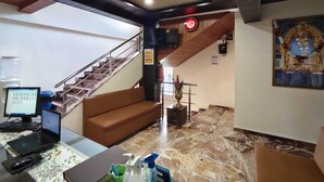 Un vestíbulo de hotel con una escalera, un sofá, un escritorio con una computadora portátil y un cartel en la pared.