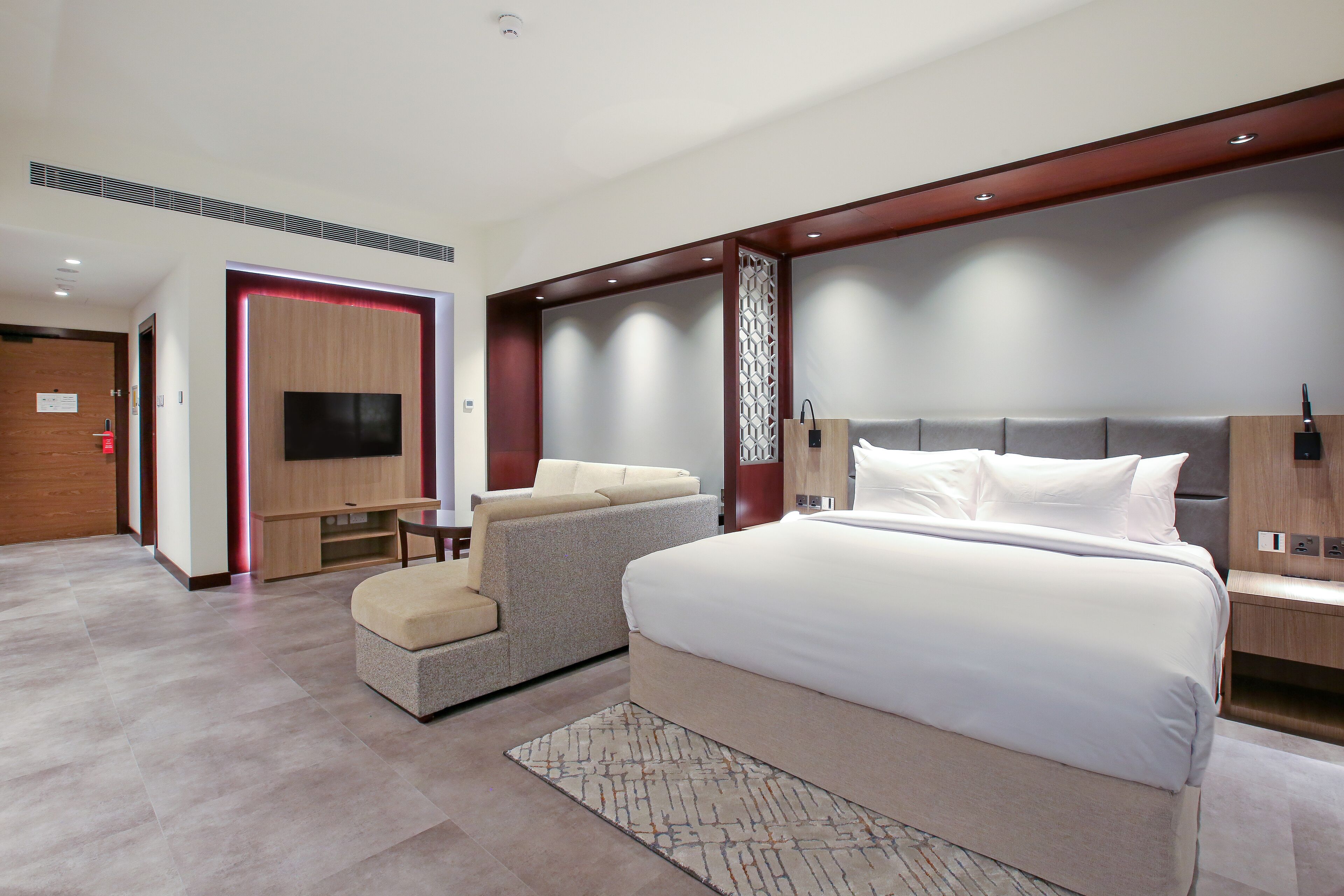 Une chambre d’hôtel moderne avec un grand lit, un canapé, une télévision et un mur décoratif en bois.