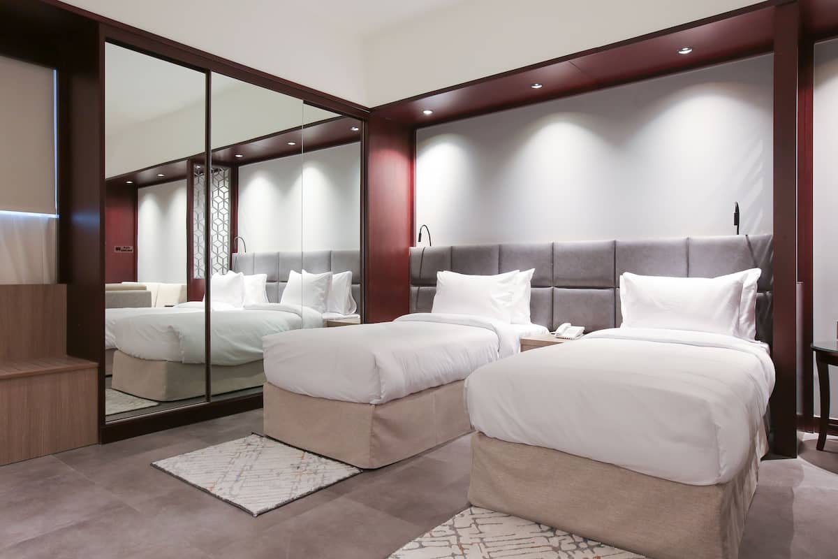 Une chambre d’hôtel moderne avec deux lits, un grand miroir et un banc en bois.