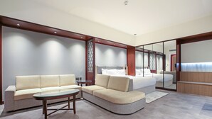 A modern hotel room with a sofa, a small table, a bed with a headboard, and a large mirror. - Sitara Hotel Apartment (Dubai)