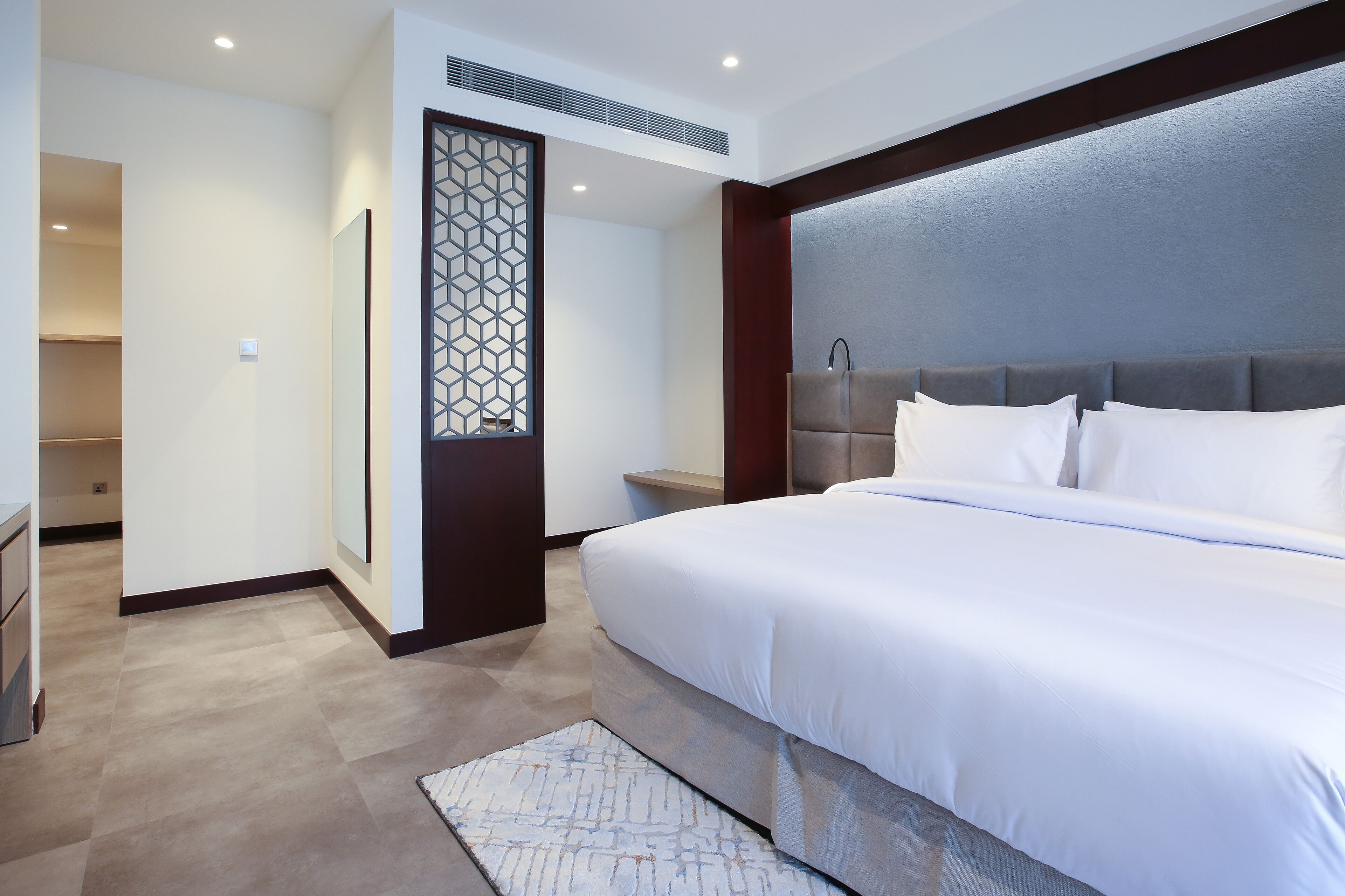 A modern hotel room with a large bed, a bedside table, a decorative screen, and a built-in headboard.