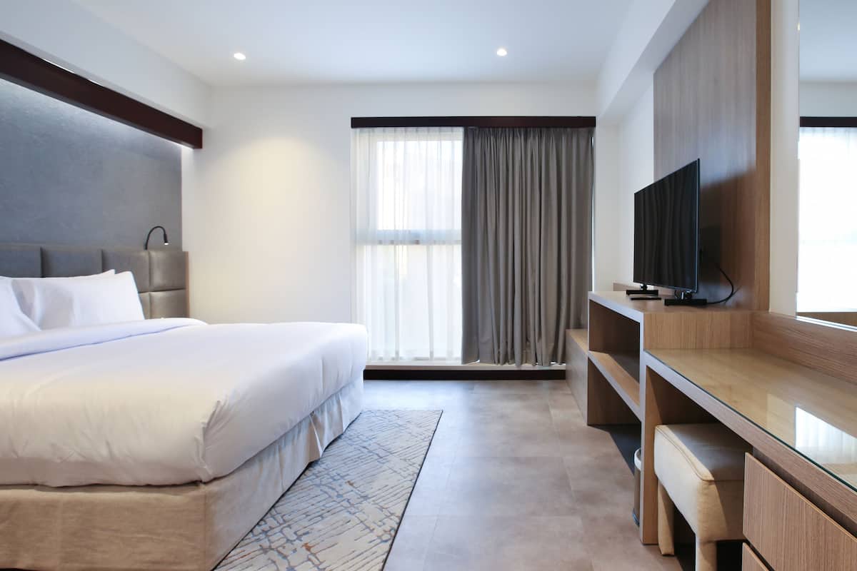 Une chambre d’hôtel moderne, dotée d’un grand lit, d’un bureau, d’une télévision et d’une fenêtre avec des rideaux.