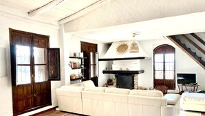 Uma sala de estar ampla com um sofá seccional branco grande, uma lareira e uma escada que leva a um andar superior.