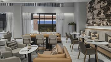 Um hall de hotel moderno com área de refeições, sofás e uma grande obra de arte na parede.