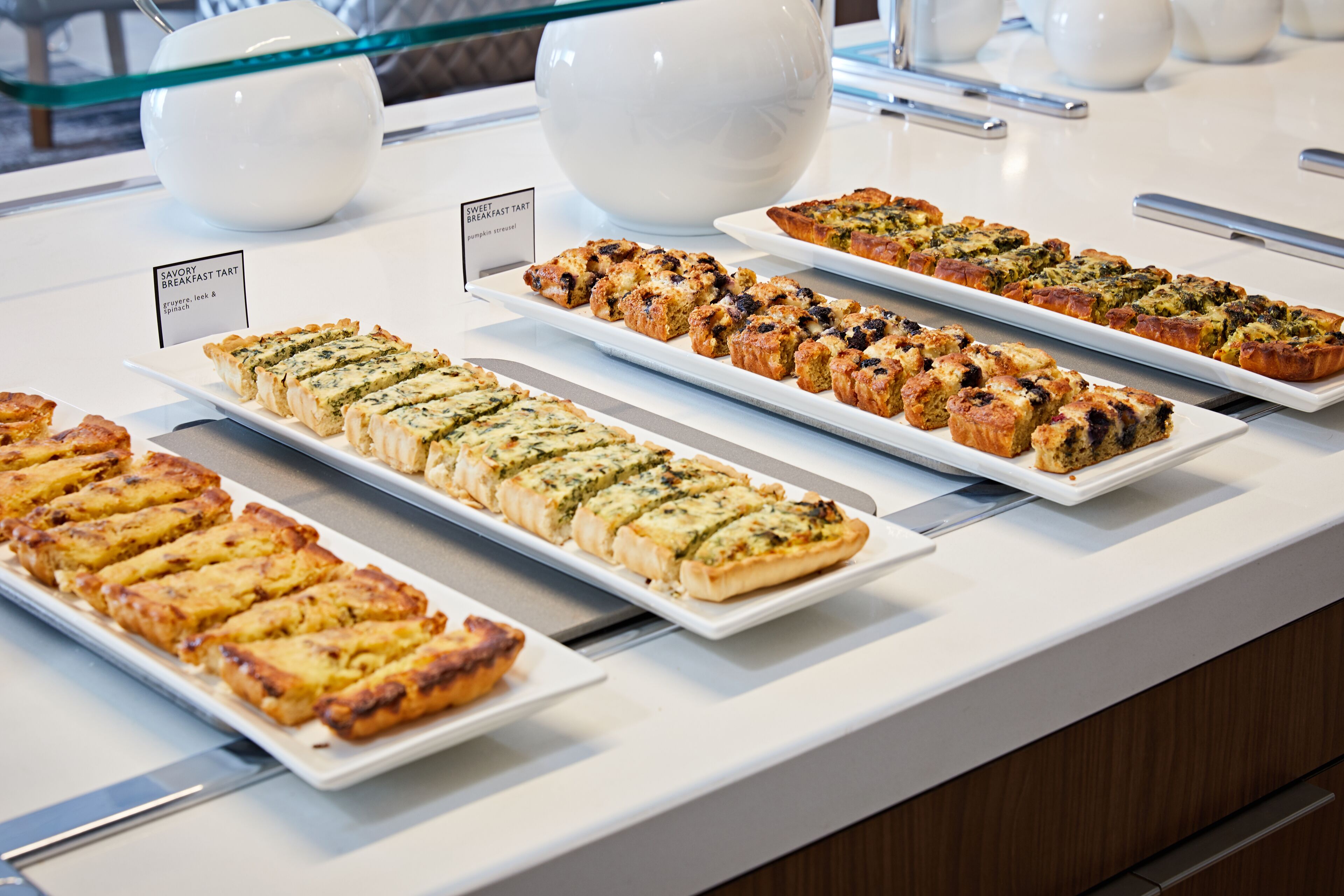 A buffet with various types of baked goods, including tarts and pastries, arranged on white serving platters.