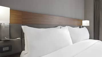Ein Hotelzimmer mit einem Holz-Kopfteil, weißer Bettwäsche, einem Nachttisch mit Lampe und einer Steckdose.