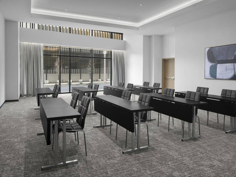 A conference room with long tables and chairs, large windows with curtains, and a modern abstract painting on the wall.