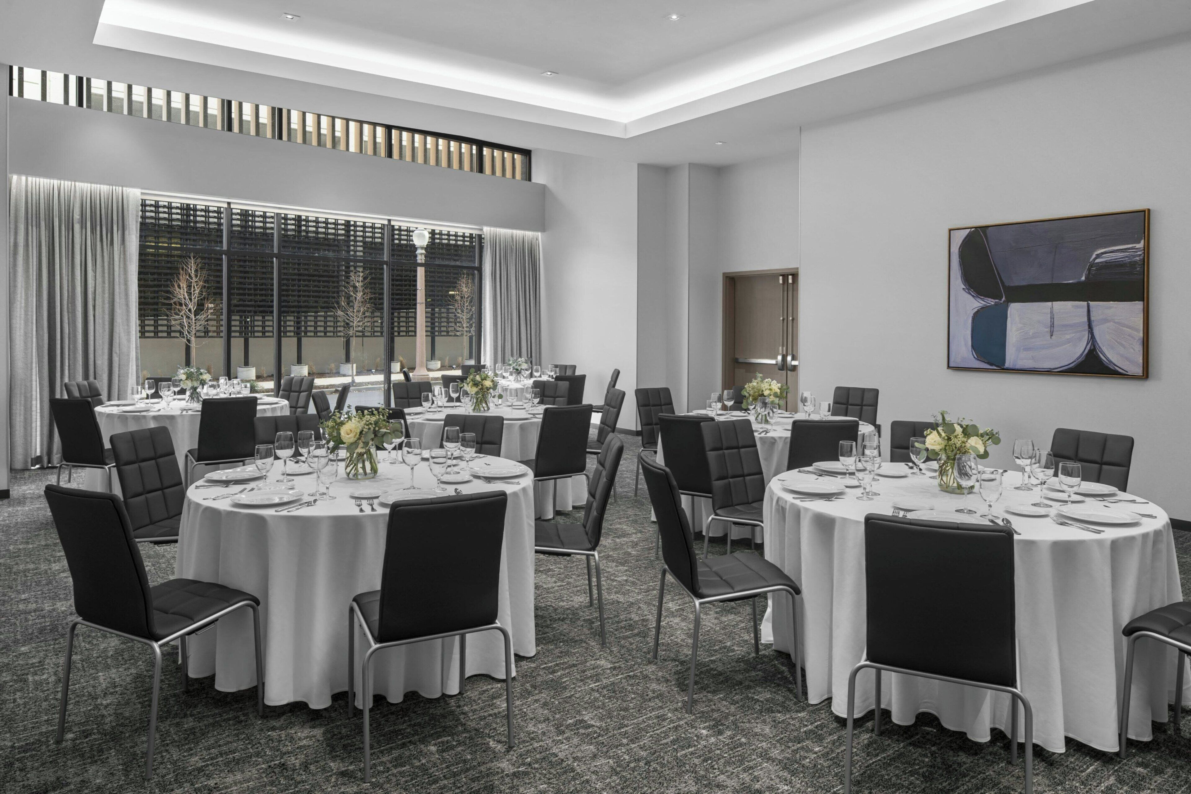 Un salón de conferencias con mesas redondas, sillas negras y manteles blancos.