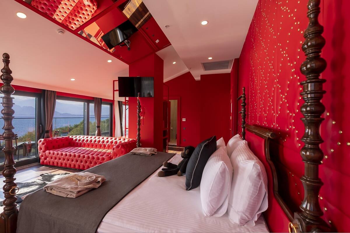 A bedroom with a large bed, a red sofa, and a view of the outdoors.