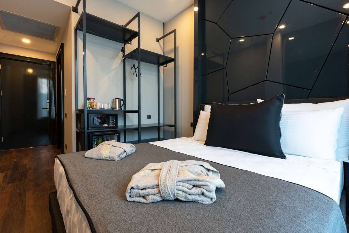 A modern hotel room with a neatly made bed, a built-in wardrobe, and a wall-mounted shelf with toiletries.