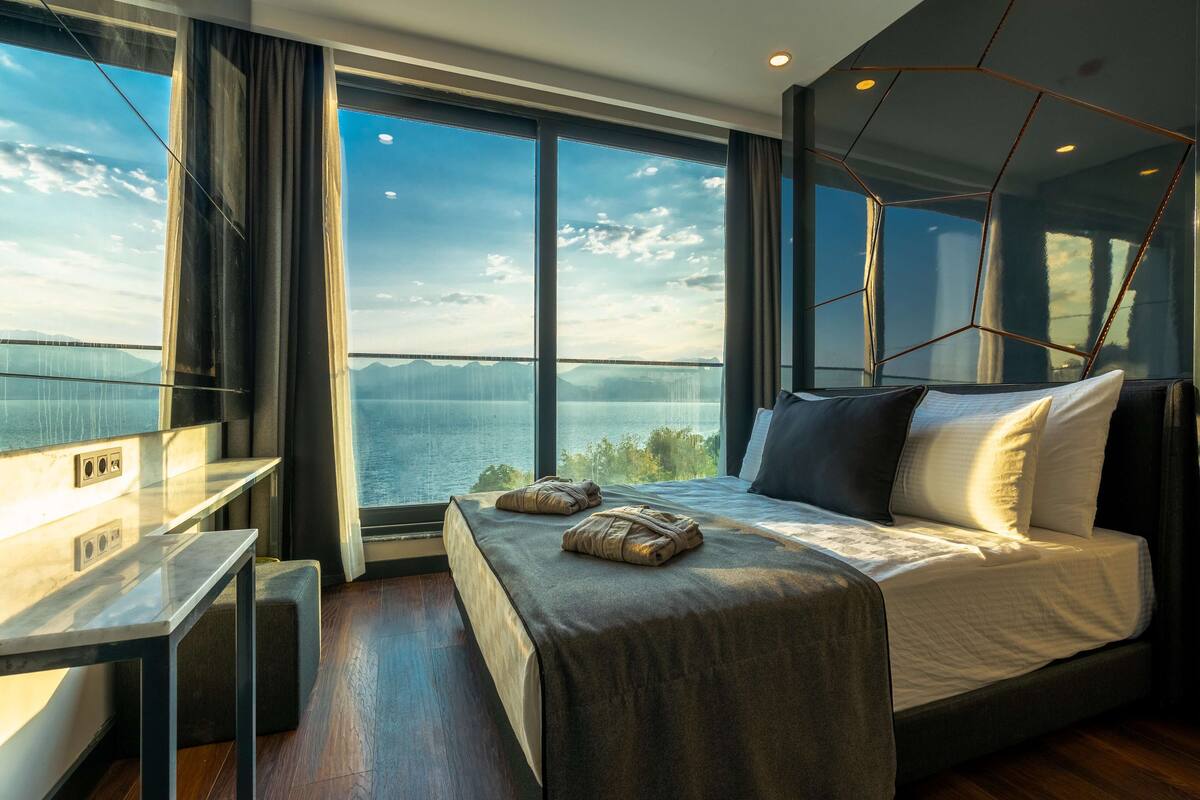 A modern hotel room with a large bed, a desk, and a view of the water.