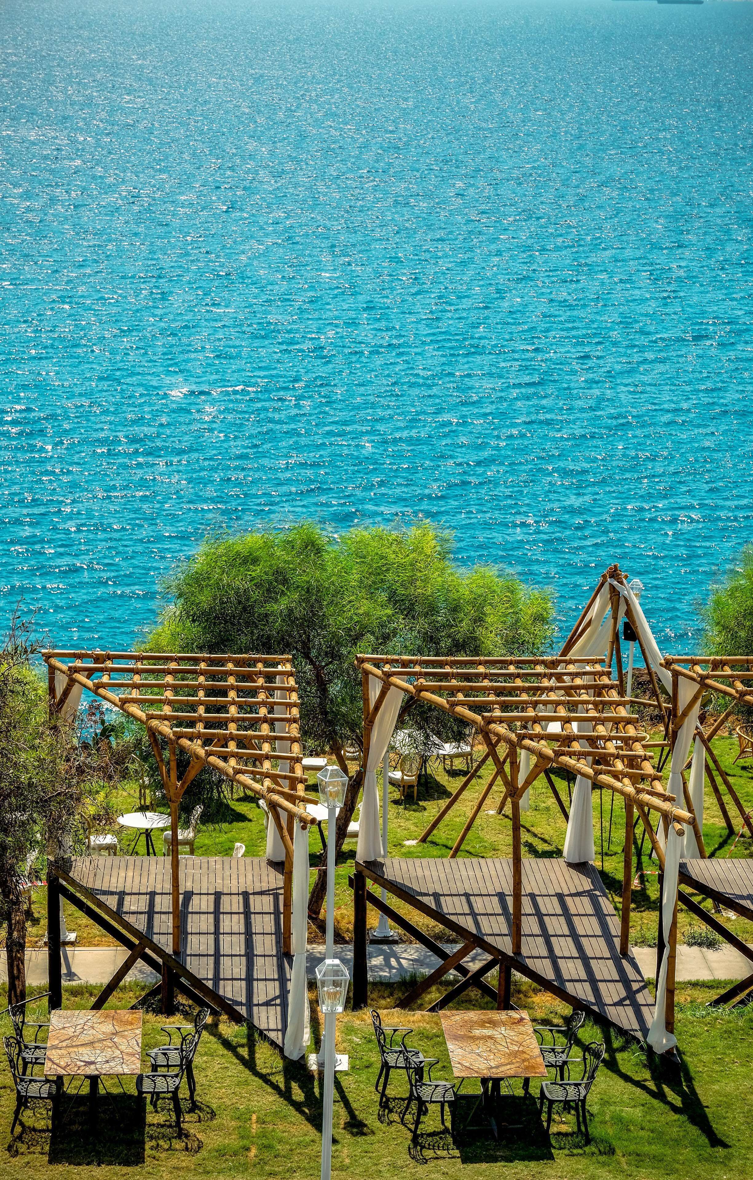 Zona de estar al aire libre con pérgolas de bambú y mesas con vistas a un cuerpo de agua.