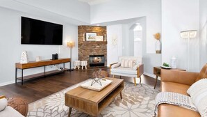 A modern living room with a large flat-screen TV, a fireplace, a sofa, and a coffee table. - ❤️Modern 4BR Joshua Tree House w/ heated Pool! (Yucca Valley)