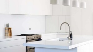 Een moderne keuken met witte kasten, een roestvrijstalen fornuis en hanglampen.